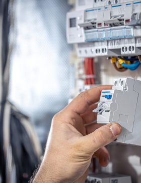Male electrician at the checkout counter on a blurred background of a switchboard.